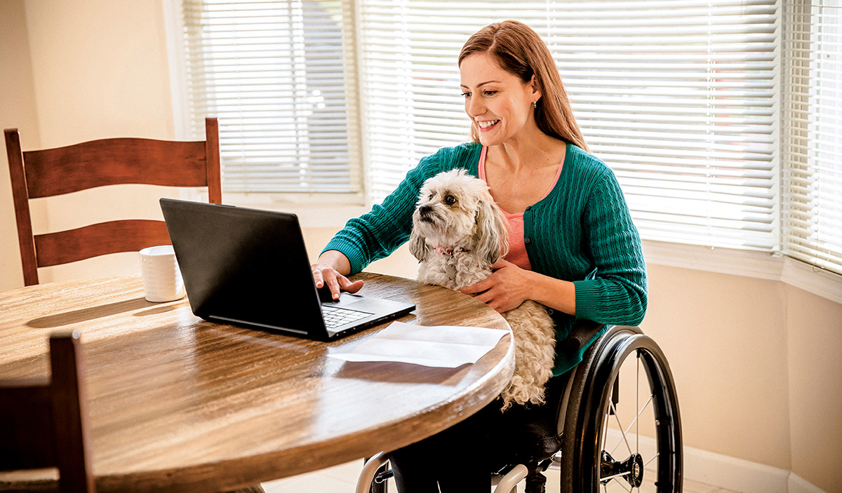 women in wheelchair with dog working on laptop