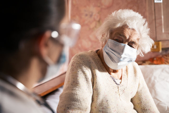 nurse talking to masked elderly woman on couch