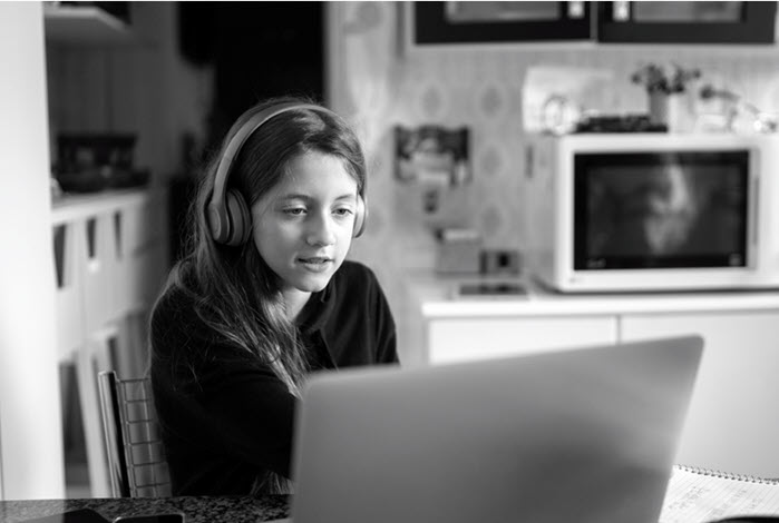 teenage girl sits in front of laptop wearing headphones