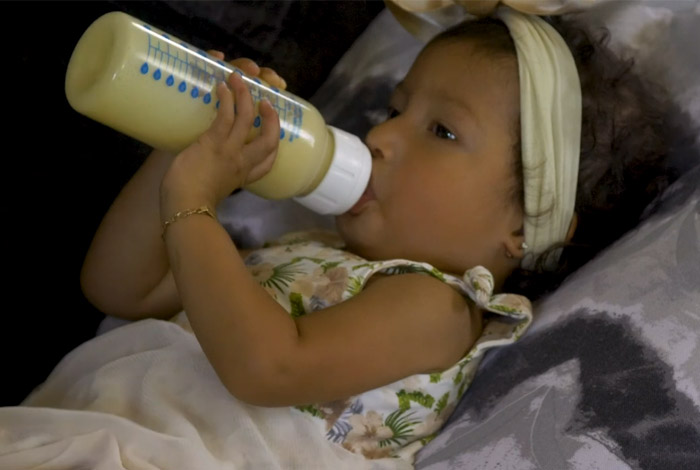 Baby feeding herself with bottle.
